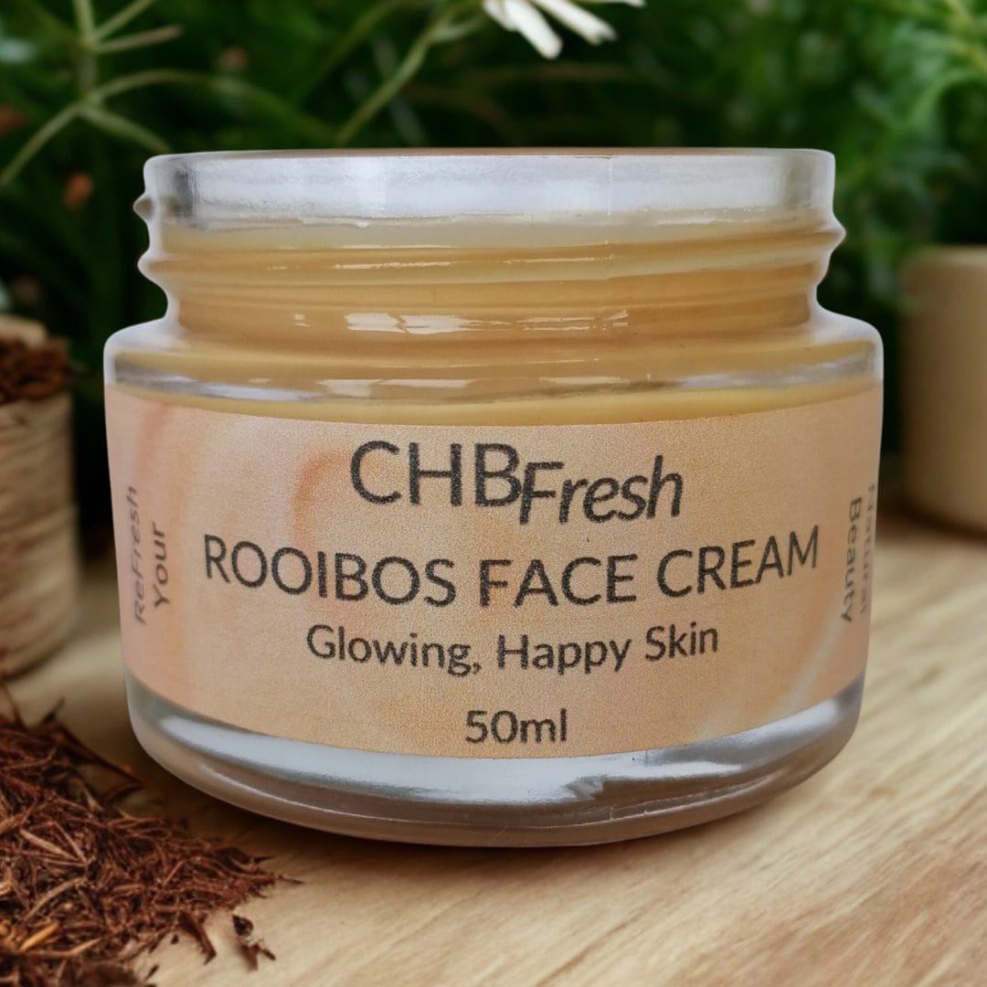 Rooibos Face Cream open jar on a wooden table with rooibos plants and tea leaves
